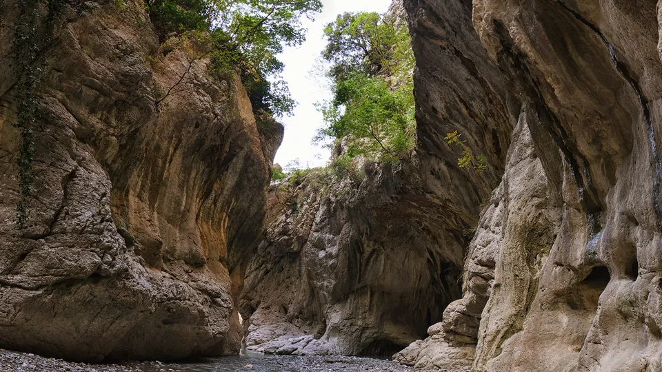 A hiker wading through the Holta River between the canyon's cliffs